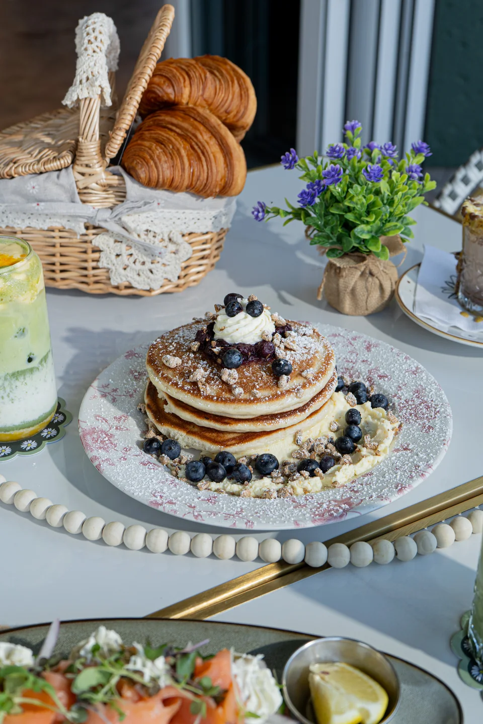 Blueberry pancakes, croissants and a matcha drink on a sunlit table at Café Bastille in Downtown Miami