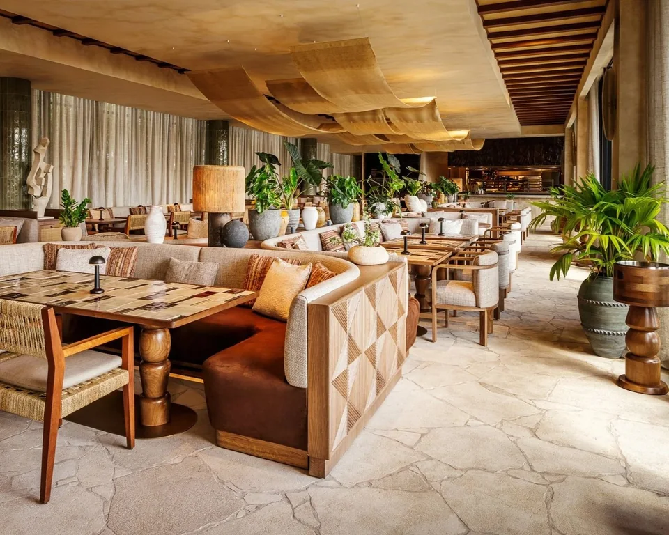 Warm wood tables, upholstered seating and tropical plants in the waterside dining space at CASA NEOS in Miami