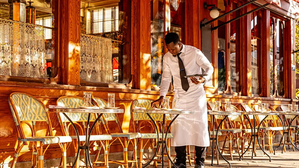 A server sets outdoor tables in warm sunlight at Le Diplomate in Washington, DC